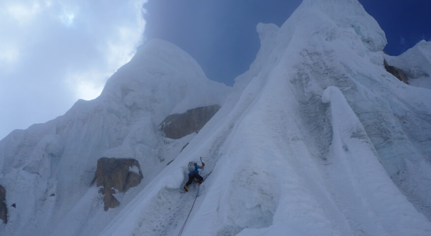 A climber on a vertical section of ice gullies leading to a summit.