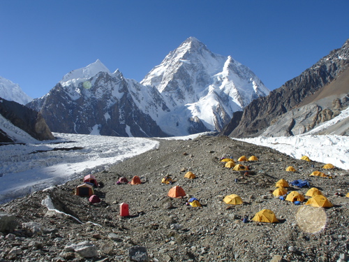 Tents on morrain terrain by the glacier, and K2 in the background.