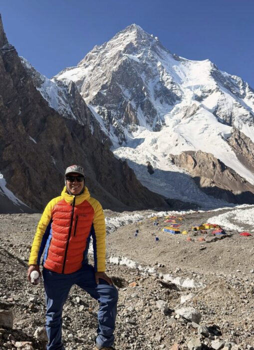 Vinayak Malli poses in front of K2, with Base Camp on a very drt glacier.