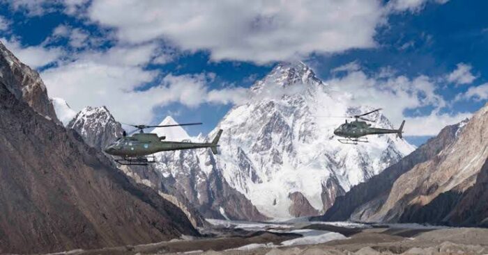 Two military helicopters, one in front of the other, in front of K2. 