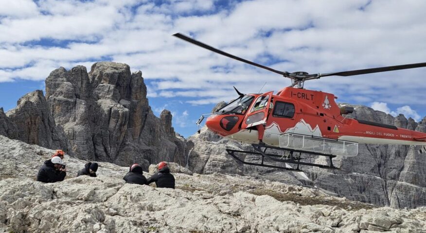 a helicdopter drops two people on a flat summit in the Dolomites.
