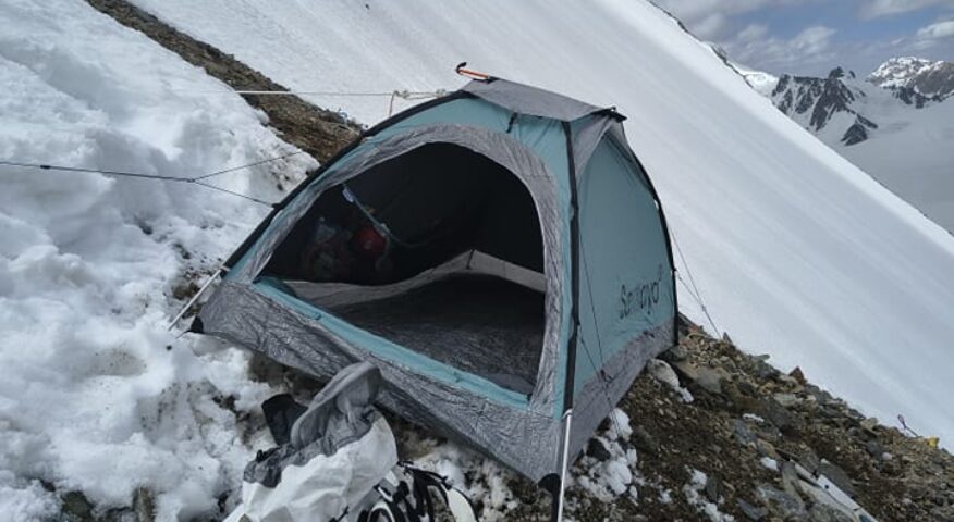 A tent on a slanted slope of snow and scree on K2