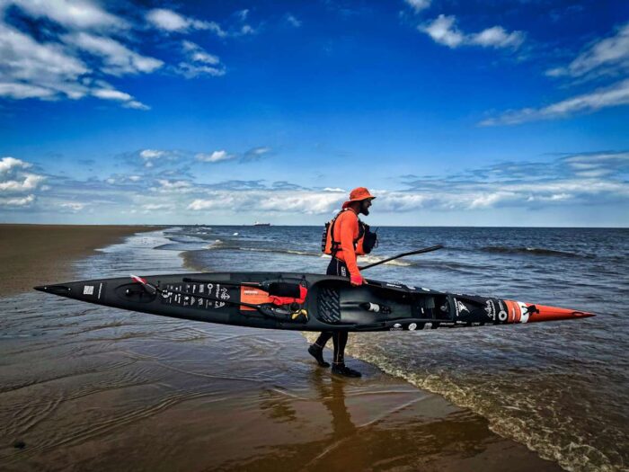 Polish adventurer Sebastian Szubski carrying his kayak into the sea on his circumnavigation of Great Britain
