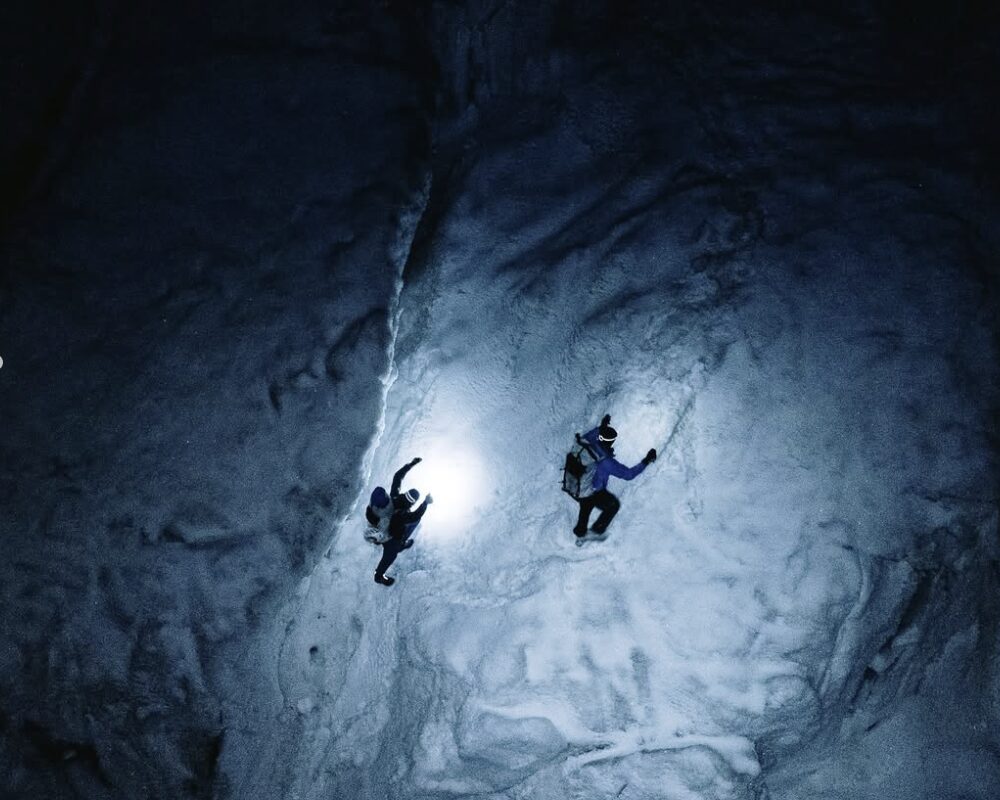 Two climbers in the night, heading up a steep snow ramp at the light of their headlamps.