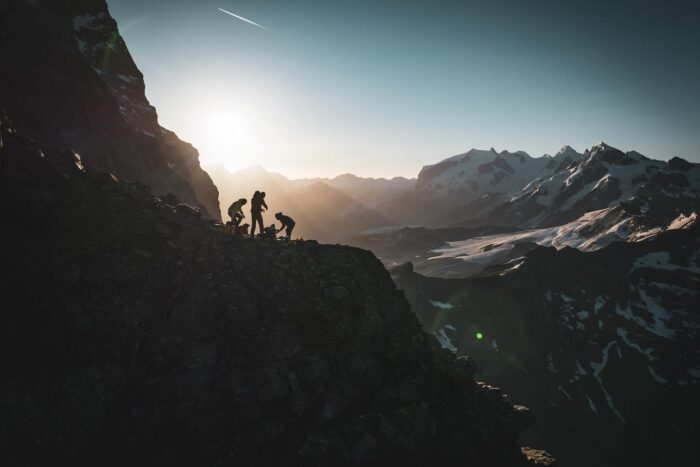 Three climbers on a rocky ledge shillouetted against the setting sun.