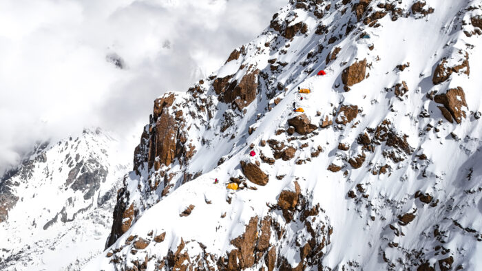 A mountain ridge with some tents scattered on the slope.