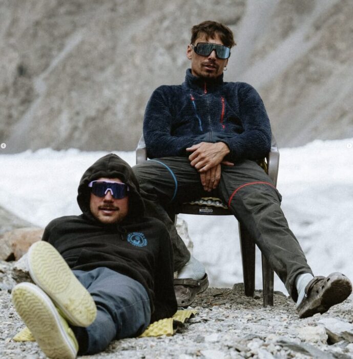 Close shot of the climbers in Base Camp, one sitting on a chair and another on the floor, with his back leaning on the chair's leg.