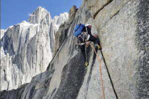 A climber on a granite all, further towers in background.