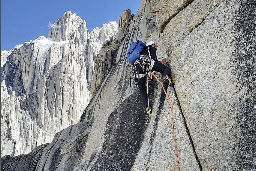 A climber on a granite all, further towers in background.
