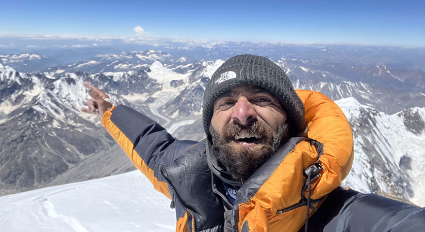 Sakhi points to mountains in background from a snowy summit.