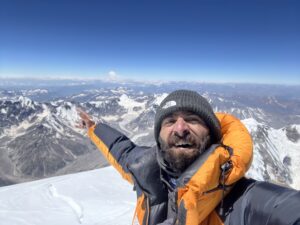 Sakhi points to mountains in background from a snowy summit.