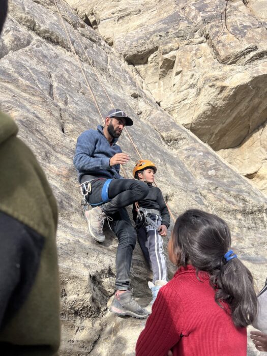 A Pakisstani guide teaches climbing skills to local kids at a climbing wall.
