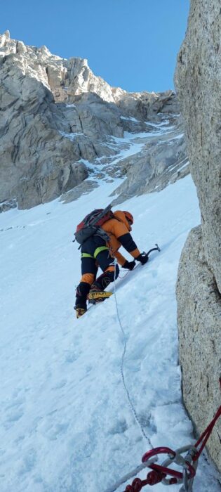 A clibmer on a steep ice-snow ramp with two ice axes.