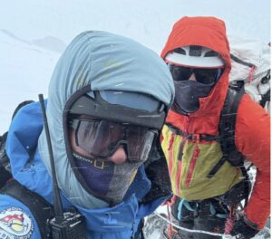 Climbers in full mountaineering gear in whiteout conditions.