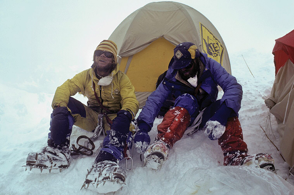 two men sitting outside their tent in the snow