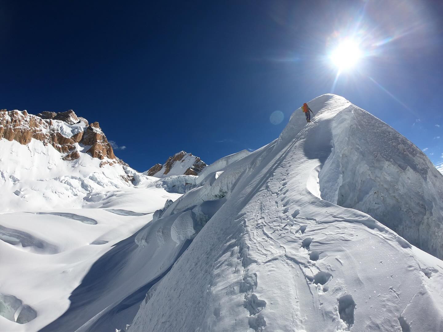 A climber approaching the top of a snow ridge, leaving only his footprints behind.