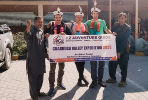 Three Polish climbers with local agents holding an expedition banner and weather local hats.