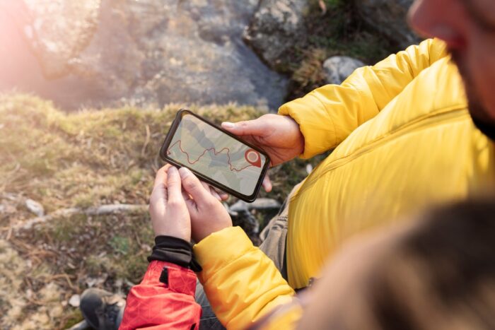 Man holding cell phone with hiking application open on the screen