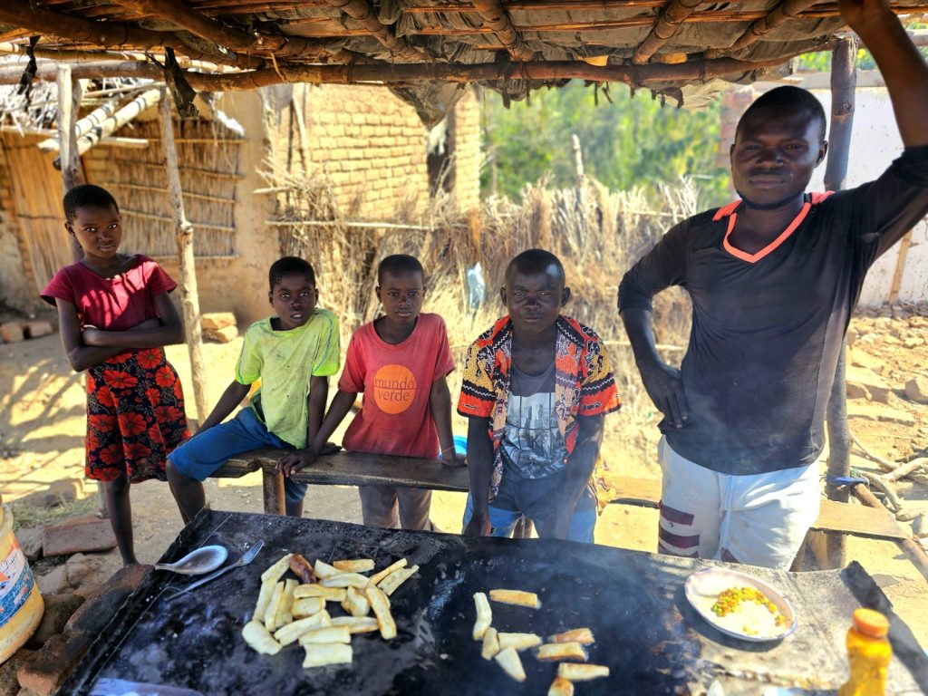 african kids and a table of food under a thatched hut