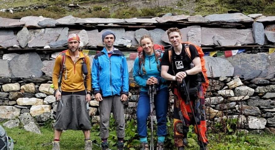 Russian team members pose standing in front of a stone wall in Nepal.