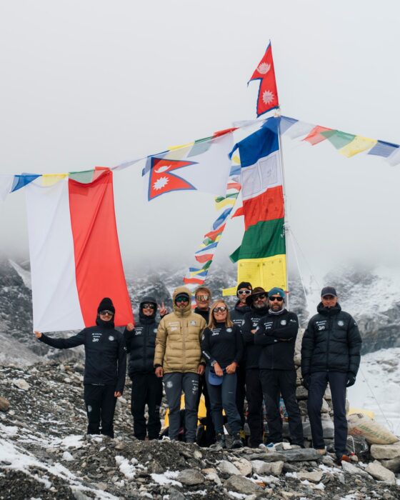 Team members stand in front of some banners at Everest Base Camp in a foggy day.