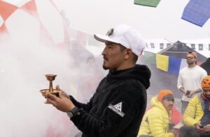 Gelje Sherpa holds a golden offering object at a base camp wrapped in the smoke of juniper bonfires.
