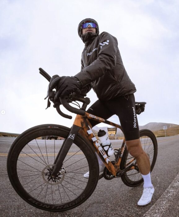 Kilian Jornet on a road bycicle, with helmet, glasses and rain jacket. 