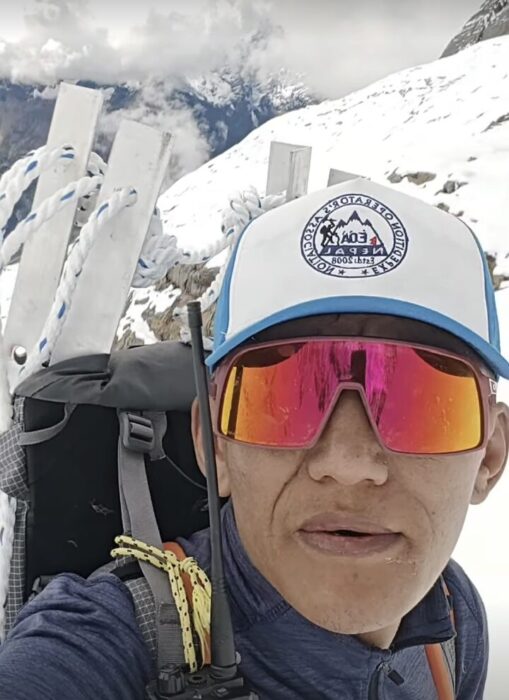 Close shot of Tashi Sherpa with cap and sunglasses, carrying ropes and snow anchors.