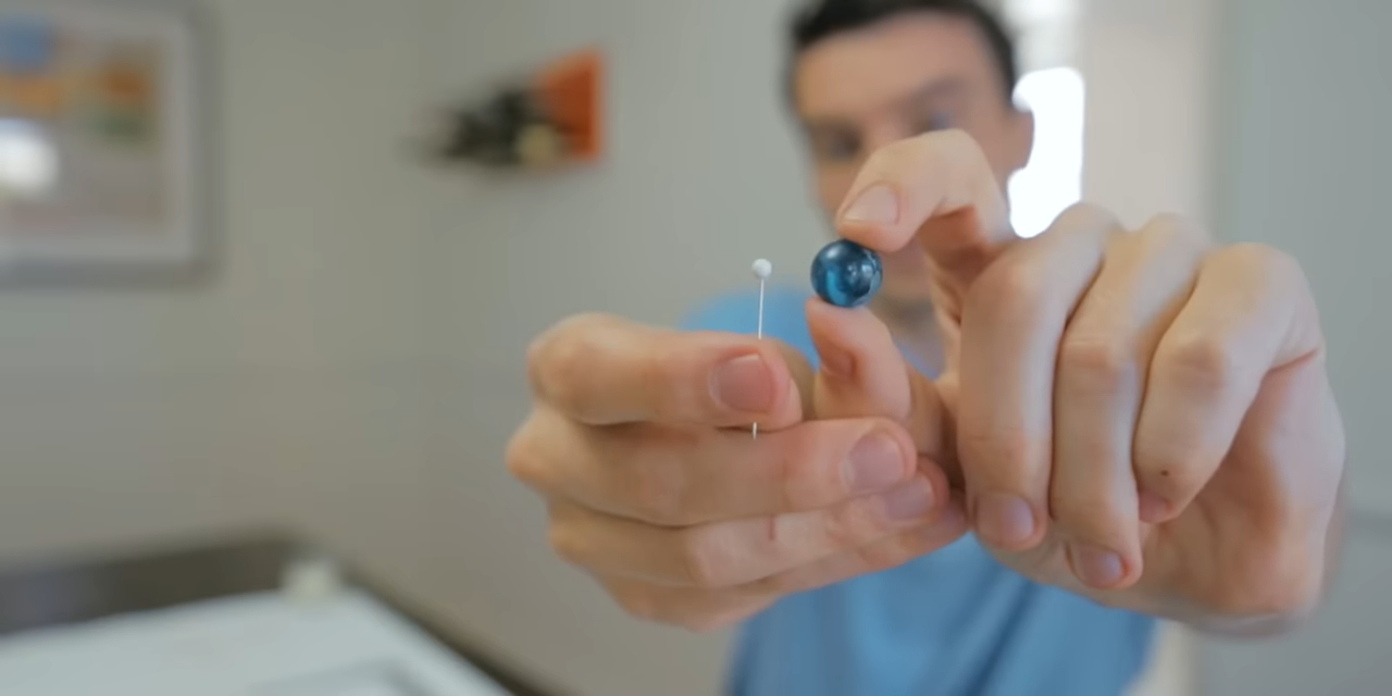 A man holding a pin and a marble up