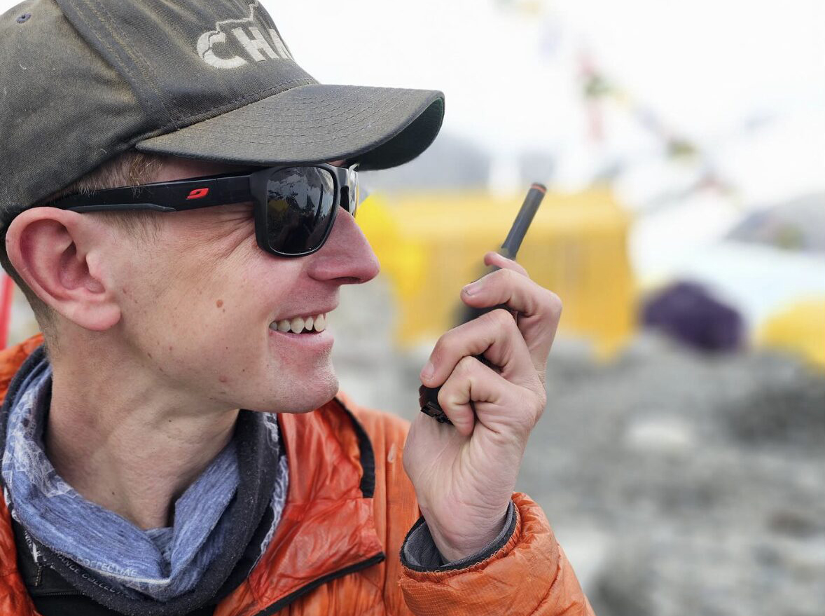 Close shot of Tyler Andrews at a rocky base camp, with an InReach device in his hand.
