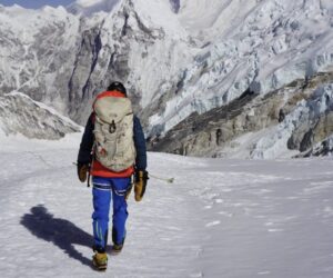 Tyler Andrews as seen from behind, walks on snow toward mouuntains in background.