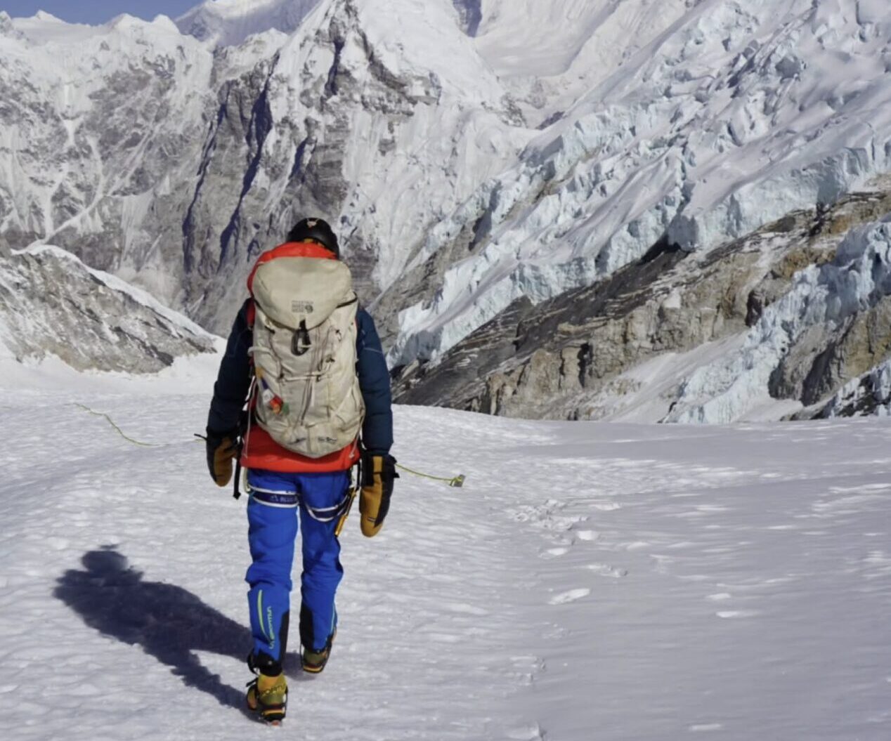 Tyler Andrews as seen from behind, walks on snow toward mouuntains in background.