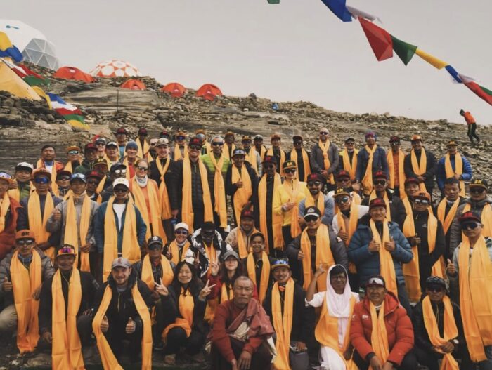 A large group of climbers pose in Base Camp with orange khata scarves