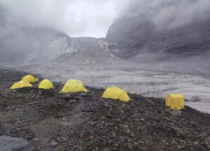 Tents on scree terrain in front of a massive col on Dhaulagiri in a foggy day.