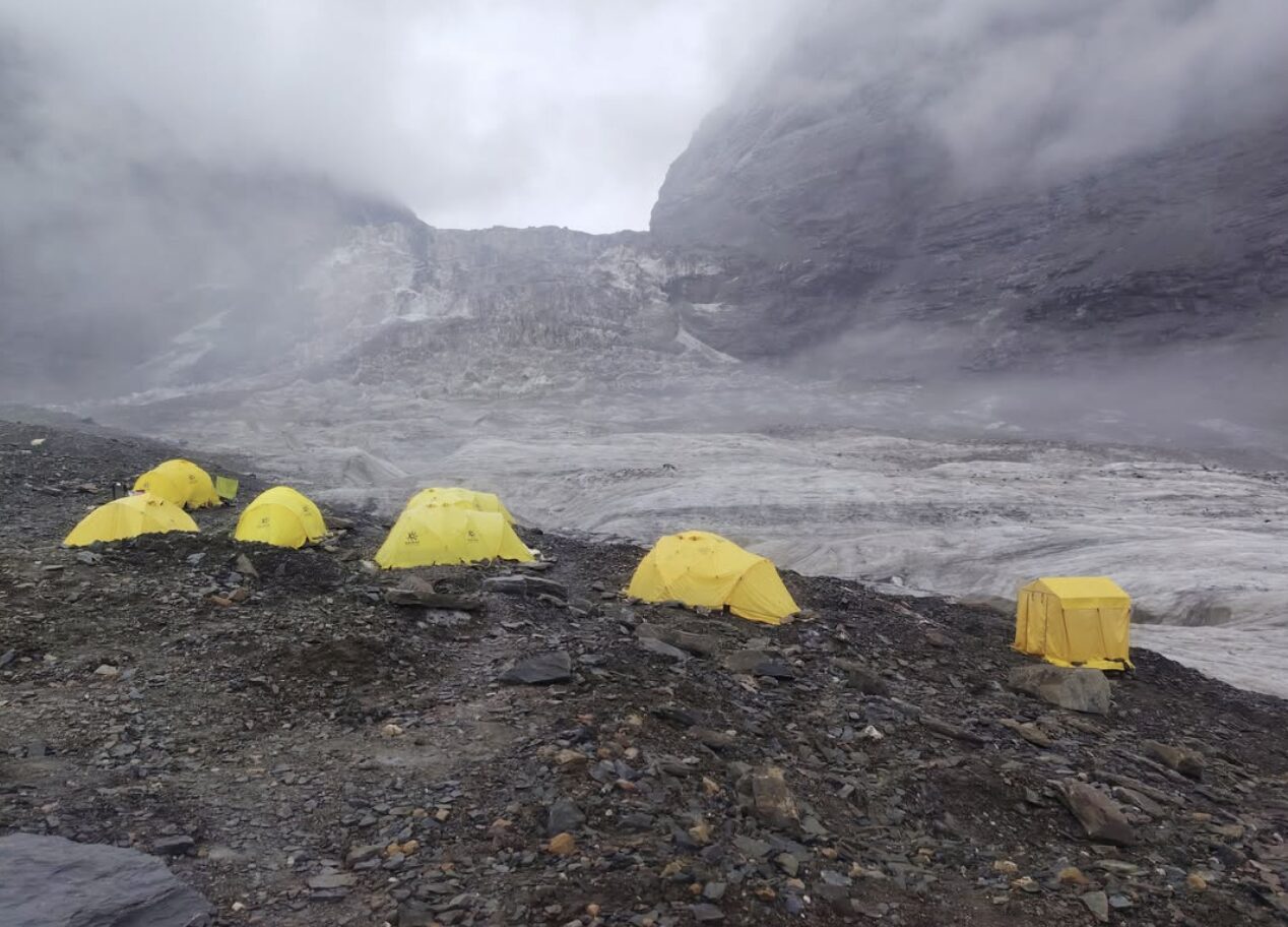 Tents on scree terrain in front of a massive col on Dhaulagiri in a foggy day.