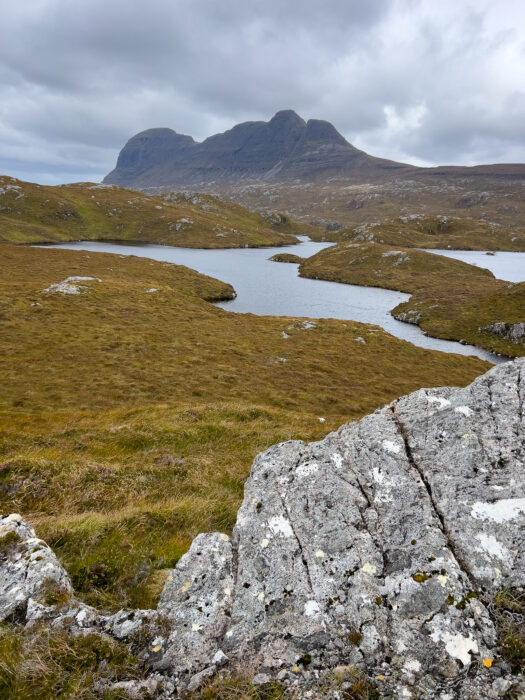 A small loch lies in front of a jagged mountain on the horizon