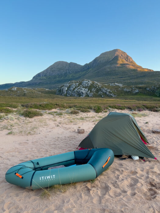 A packraft and tent on a beach, with a mountain in the background