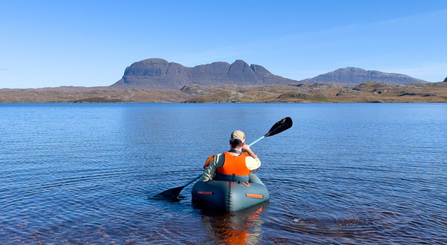Man paddles packraft on calm waters with mountain in the distance