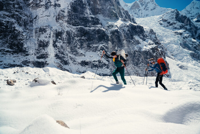 The climbers walk on soft snow with walking poles.