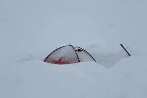 A tent half buried in fresh snow in the whiteout.