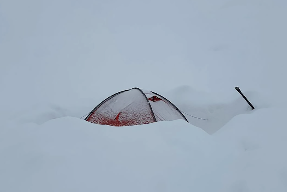 A tent half buried in fresh snow in the whiteout.