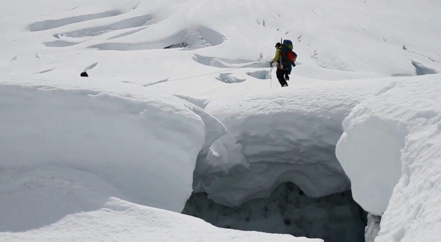 A crevasse and several men hiking past