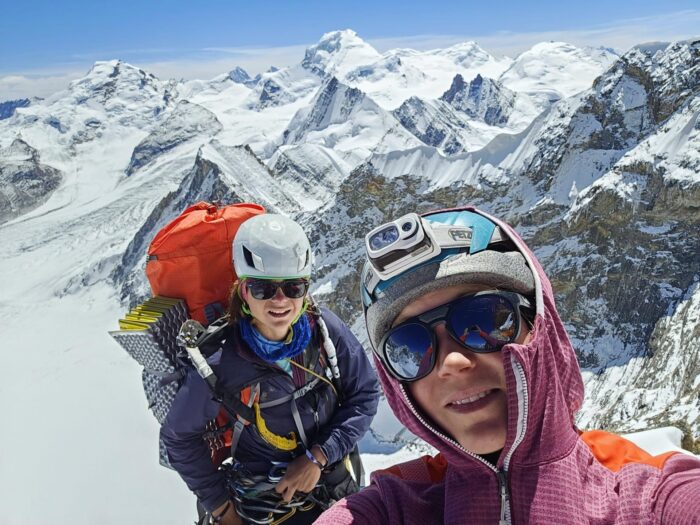 Selfie by two Slovenial female climbers, with climbing helmets and sunglasses.