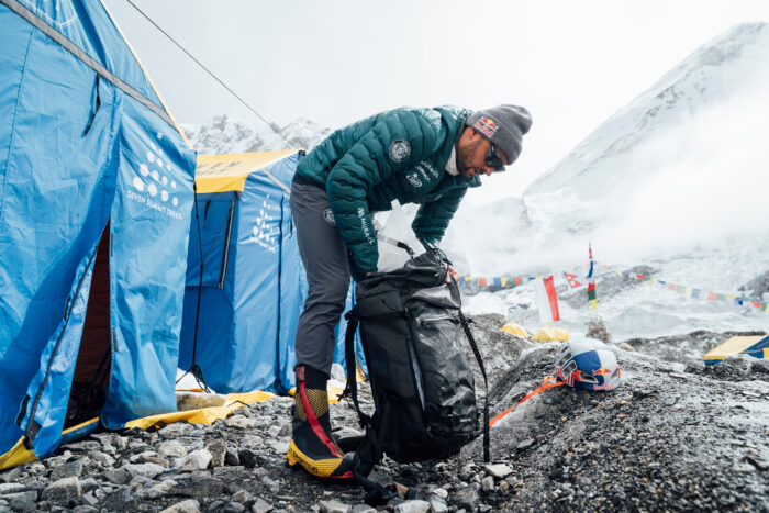 Bargiel stuffs gear in a backpack, in front a line of tents in Everest BC.