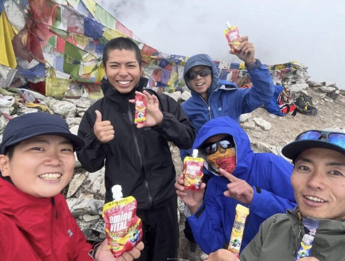 Young Japanese climbers on a rocky summit, posing with tubes of fruit gel in their hands.