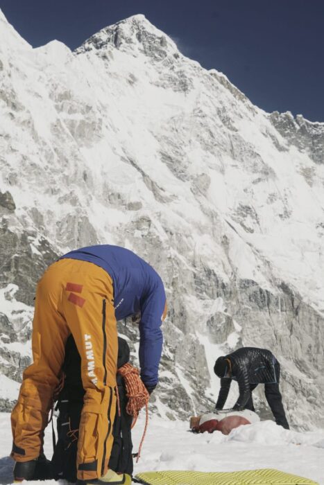 Two climbers pick gear from their backpacks, at a flat spot in front of Cho Oyu's south face.