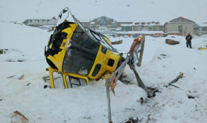 A crashed helicoper on snowy ground with buildings of a village behind.