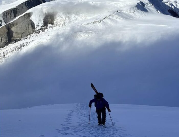 A climber on a snow slope with skis on his back .