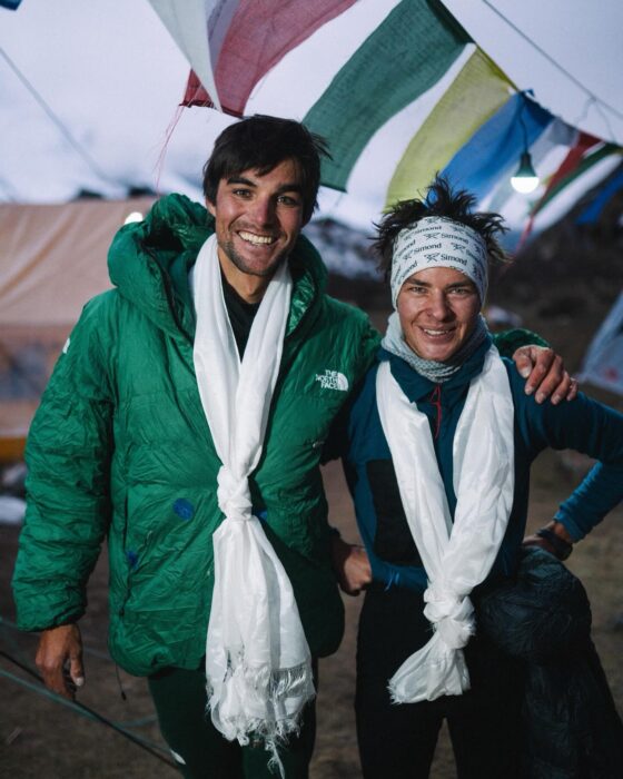 Vedrines and Jean smile tot he cmaera with green dawn jackets and white khata scarves around their necks.