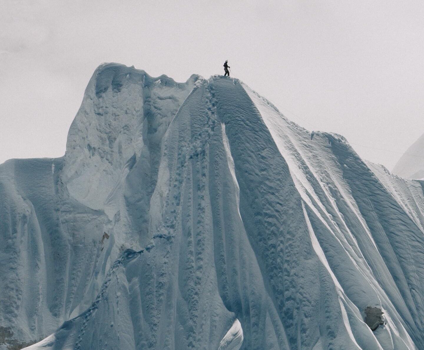 The shillouette of a climber on the top of a huge snow cornice.